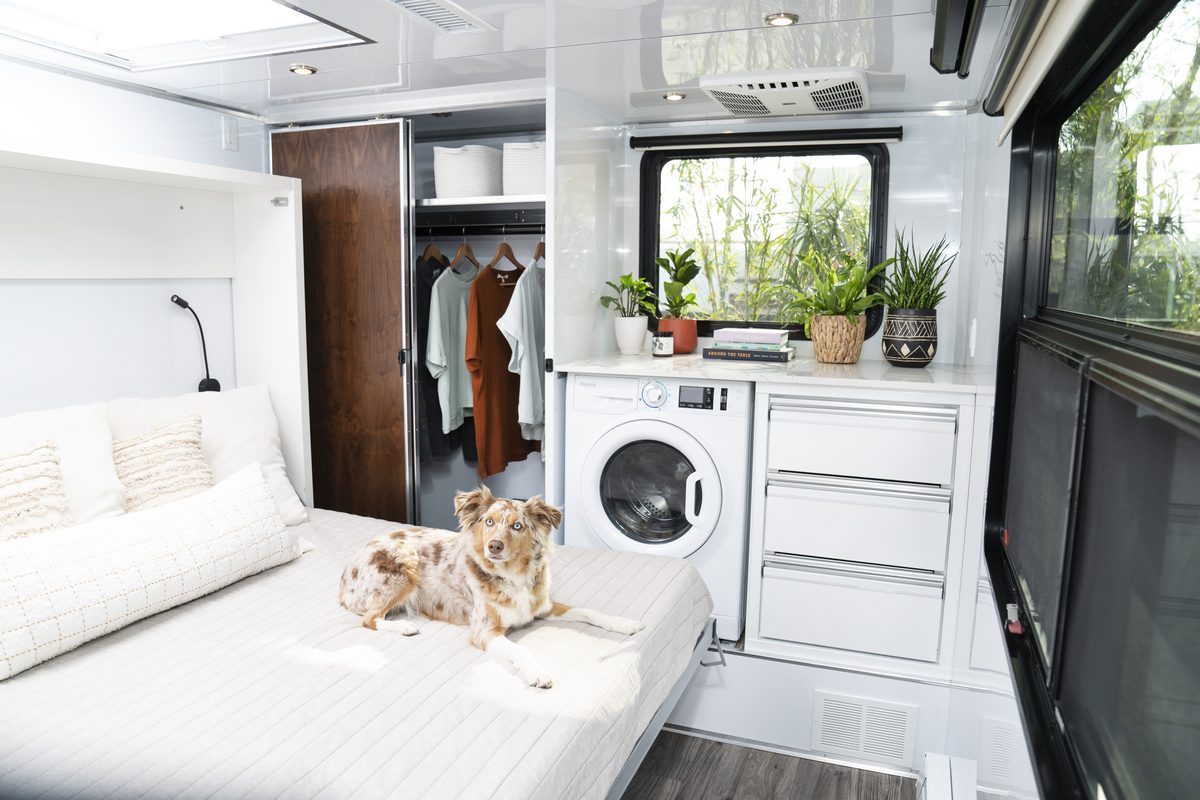 Inside a Living Vehicle HD29: the bed, a closet and a washer, with two dogs on the bed