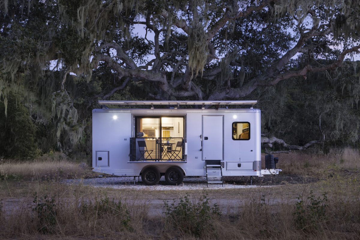 A Living Vehicle travel trailer at dusk under a large oak tree