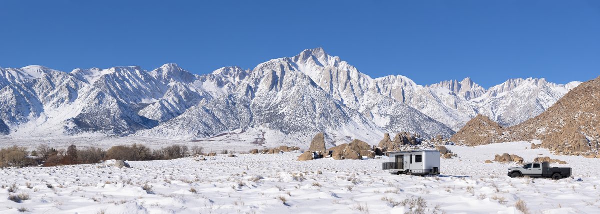 A truck and a Living Vehicle travel trailer in the snow below the Sierra Nevada