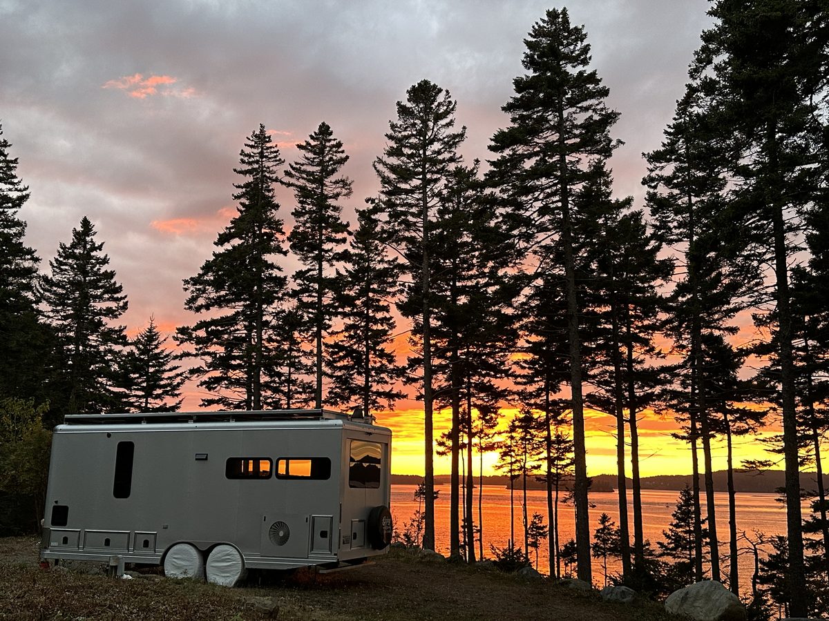 A Living Vehicle among pine trees at a lakeside sunset